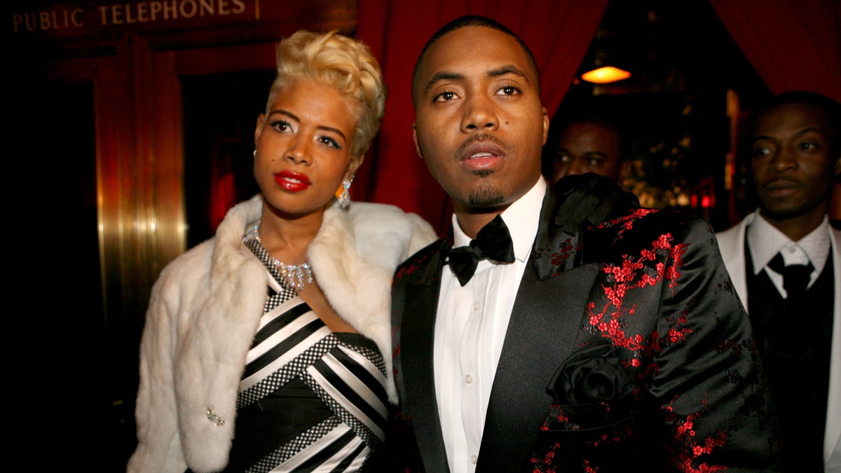 Nas wearing a black and red suit jacket and Kelis wearing a white and black dress